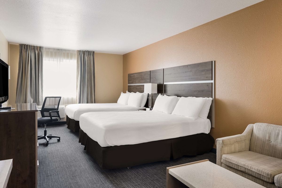 A hotel room with two beds, a desk, a chair, and a sofa.