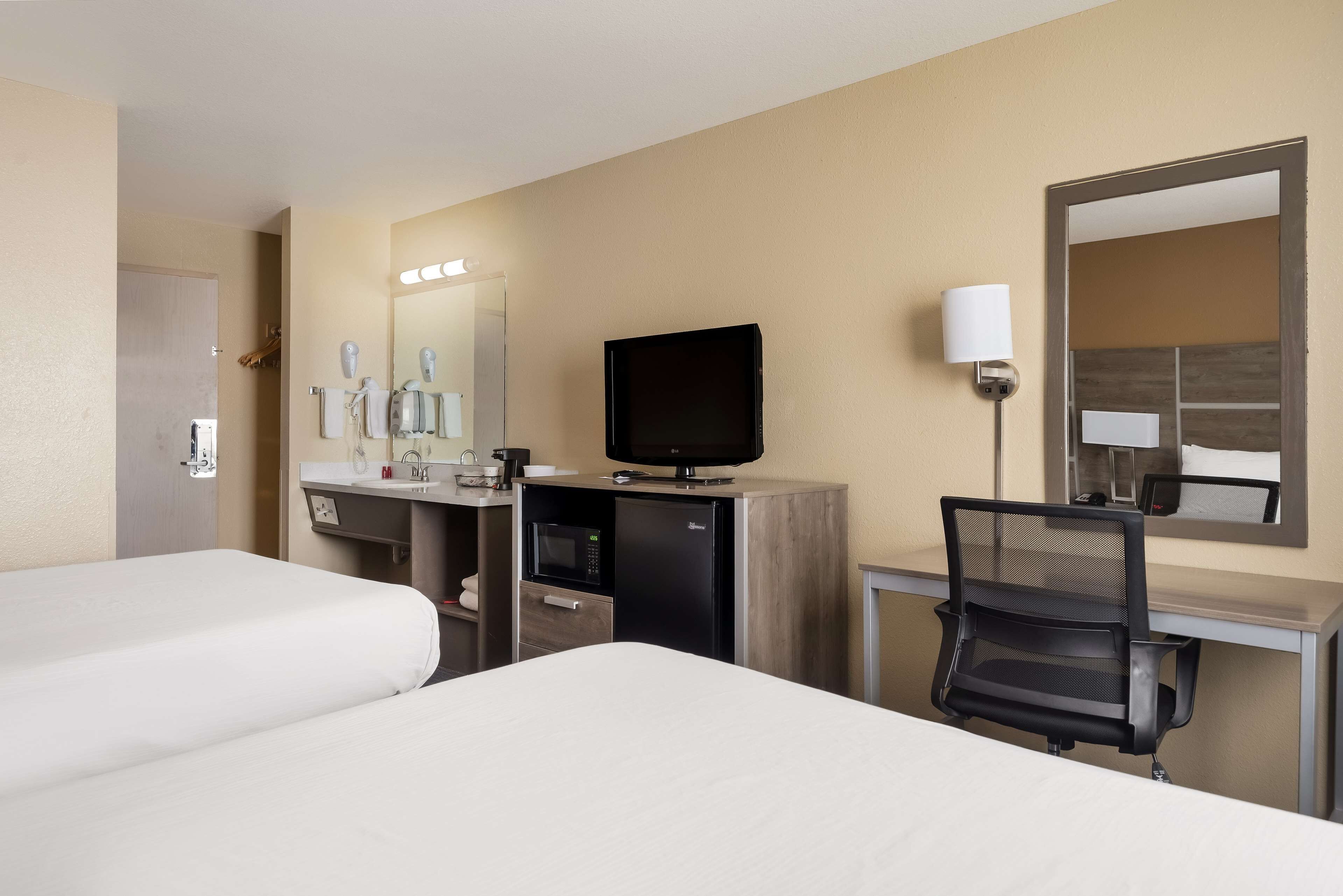 Une chambre d’hôtel avec deux lits, un bureau avec un ordinateur, un four à micro-ondes et une télévision.