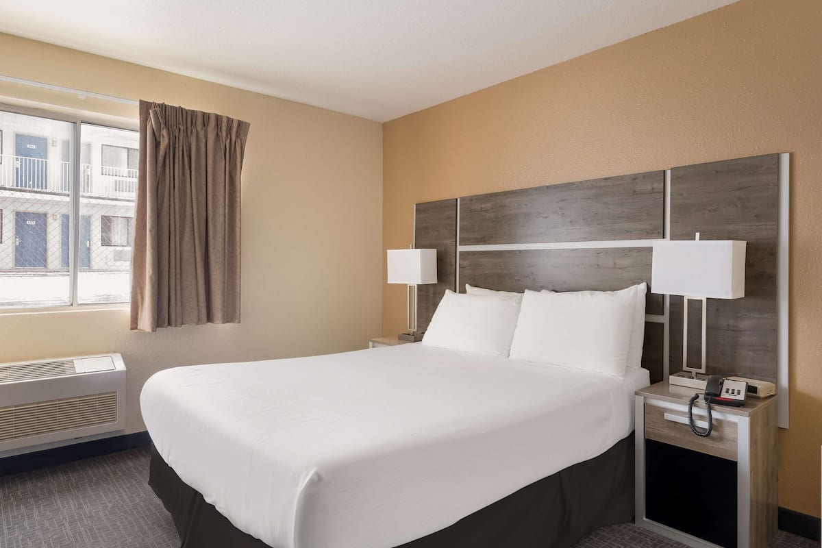 A hotel room with a large bed, two bedside lamps, a nightstand with a phone, and a window with curtains.