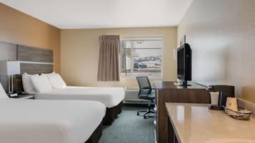 Quarto de hotel com duas camas, uma escrivaninha com computador, televisão e janela com vista para montanhas.