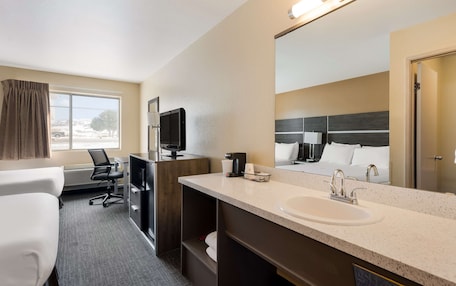 A hotel room with a large bed, a desk, a chair, a TV, a sink, and a mirror.