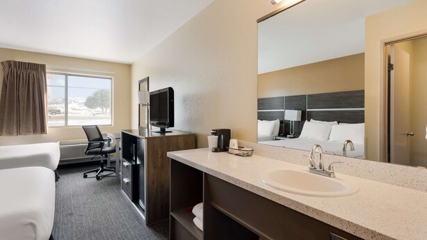 A hotel room with a large bed, a desk, a chair, a TV, a sink, and a mirror.