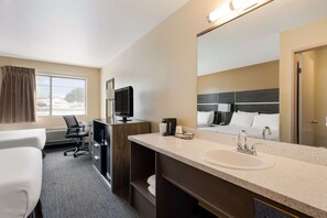 Ein Hotelzimmer mit einem großen Bett, einem Schreibtisch, einem Sessel, einem Fernseher, einem Waschbecken und einem Spiegel.
