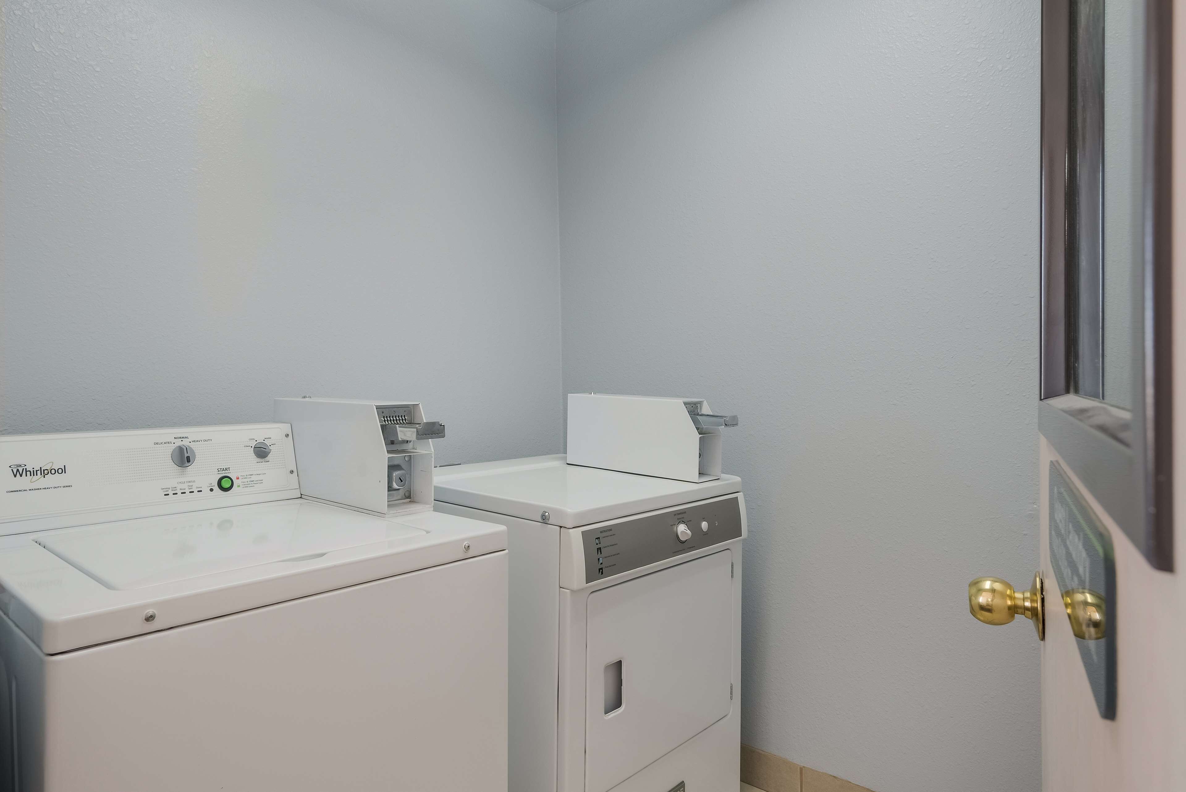 A laundry room with two Whirlpool washers and dryers, a door with a brass handle, and a light switch on the wall.