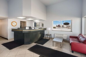 A modern hotel lobby with a reception desk, a red leather sofa, a coffee table, a clock, and a large window with a city view.