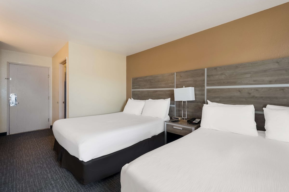 A hotel room with two beds, a nightstand with a lamp, and a door.