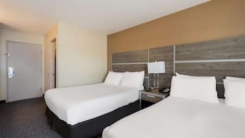 A hotel room with two beds, a nightstand with a lamp, and a door.