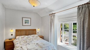 Un dormitorio con cama, mesitas de noche, una ventana con cortinas, un cuadro en la pared y una lámpara en el techo.