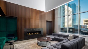 A modern living room with a fireplace, a sectional sofa, and a large window offering a city view. - Deedee's Sky Rise Apartments - Newport 2 (Jersey City)