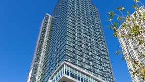 A tall, modern glass building with a clear sky in the background. - Deedee's Sky Rise Apartments - Newport 2 (Jersey City)