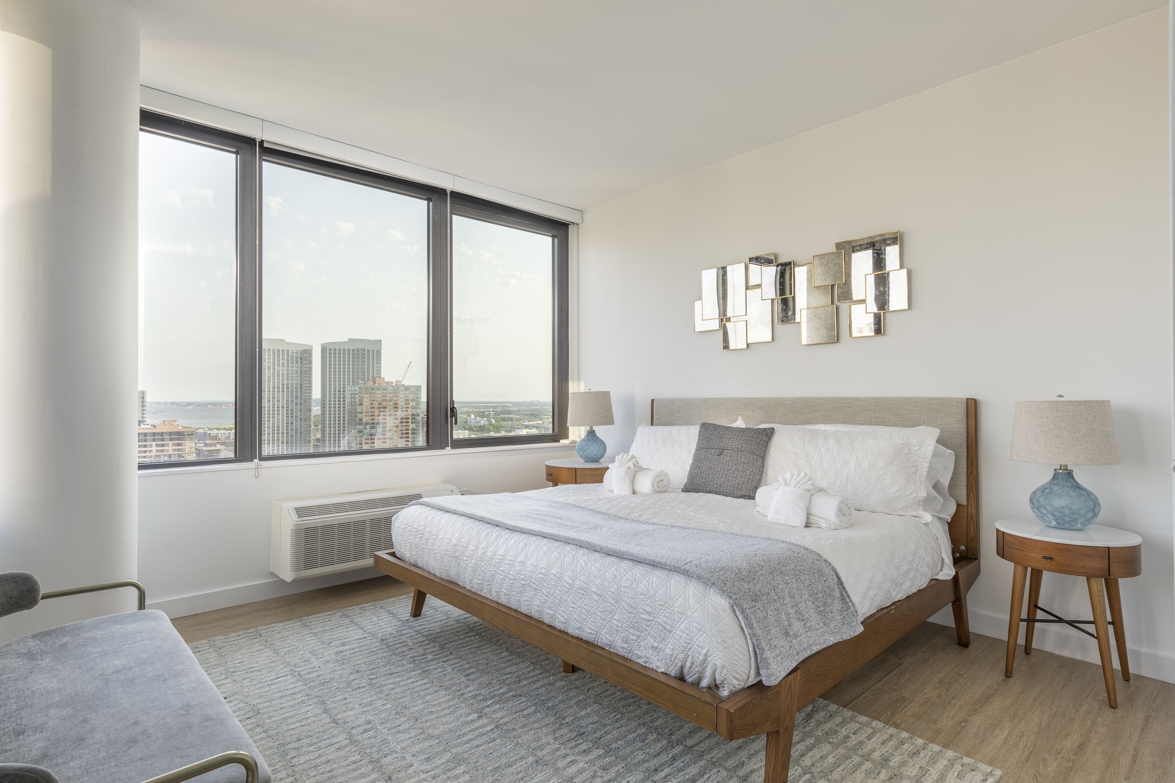 A modern bedroom with a large bed, a view of the city, and a cityscape through the window.