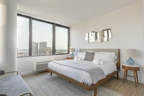 A modern bedroom with a large bed, a view of the city, and a cityscape through the window.