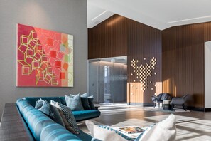 A modern lobby with a teal sofa, abstract art, a wooden wall feature, and a glass door leading to another area.