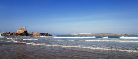 A beach with clear skies, waves, and rocky formations.