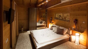 A cozy wooden cabin bedroom with a large bed, a mirror, and a bedside table with a lamp. - Lakefront Villa Jelenic By Bertovic in Croatia with a squash court, gym, cinema (Ogulin)
