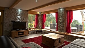 A cozy living room with a stone wall, wooden beams, a television, a bench, and a large window with red curtains. - Lakefront Villa Jelenic By Bertovic in Croatia with a squash court, gym, cinema (Ogulin)