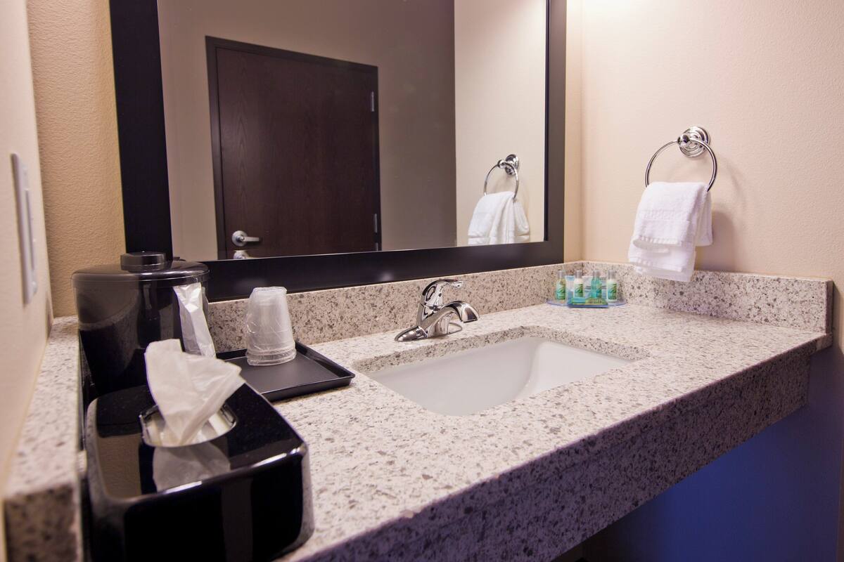 A hotel bathroom with a granite countertop, a sink, a mirror, and a towel rack.