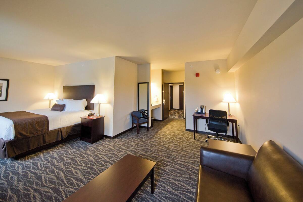 A hotel room with a bed, bedside tables, a desk, a chair, a sofa, and a carpeted floor.