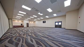 A large, carpeted room with a patterned floor, multiple ceiling lights, and a door with an exit sign.
