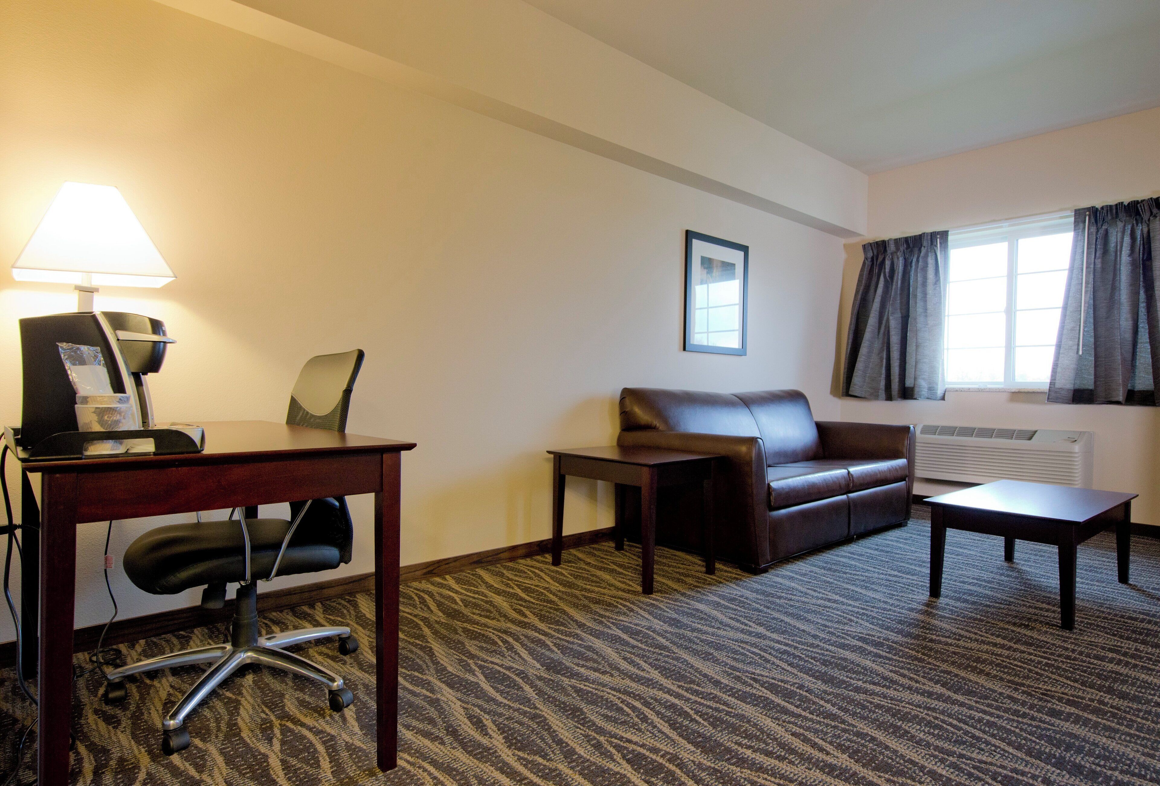 Una habitación de hotel con escritorio, silla de oficina, sofá de cuero y una mesita.