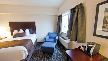 A hotel room with a bed, a chair, a desk with a coffee maker, and a window with curtains.