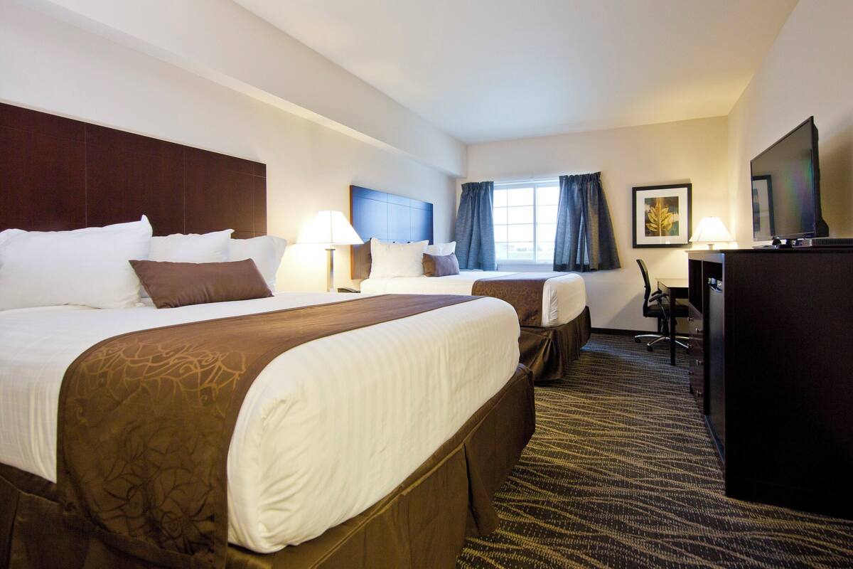 A hotel room with two beds, a desk, a television, and a window with curtains.