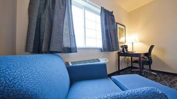 A hotel room with a blue patterned sofa, a desk with a lamp, and an air conditioning unit.