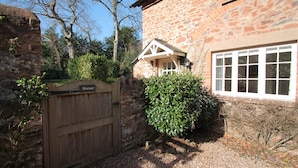 A stone building with a wooden gate, a window, and a hedge. - Horner Cottage, Luccombe (Nr Porlock)