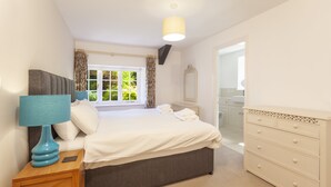 A bedroom with a bed, bedside table, lamp, dresser, and a window with curtains. - Horner Cottage, Luccombe (Nr Porlock)