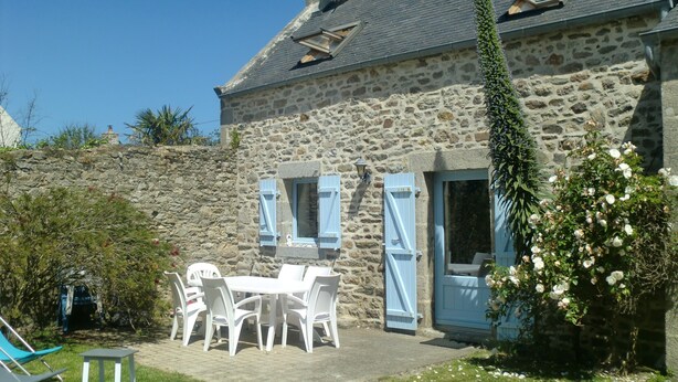 Una casa in pietra con un muro di pietra, un giardino con tavolo e sedie, e una porta blu.