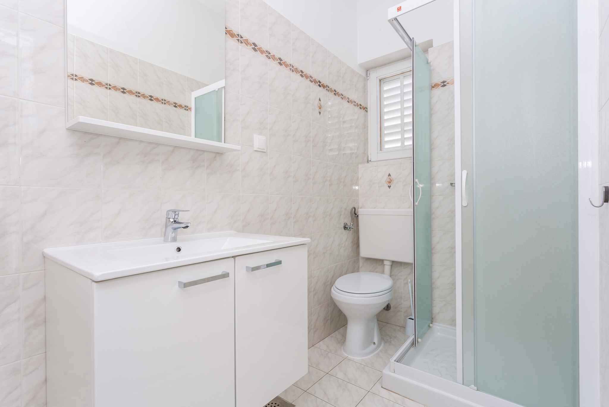 Une salle de bain avec un lavabo blanc, des toilettes et une douche fermée par des parois en verre.