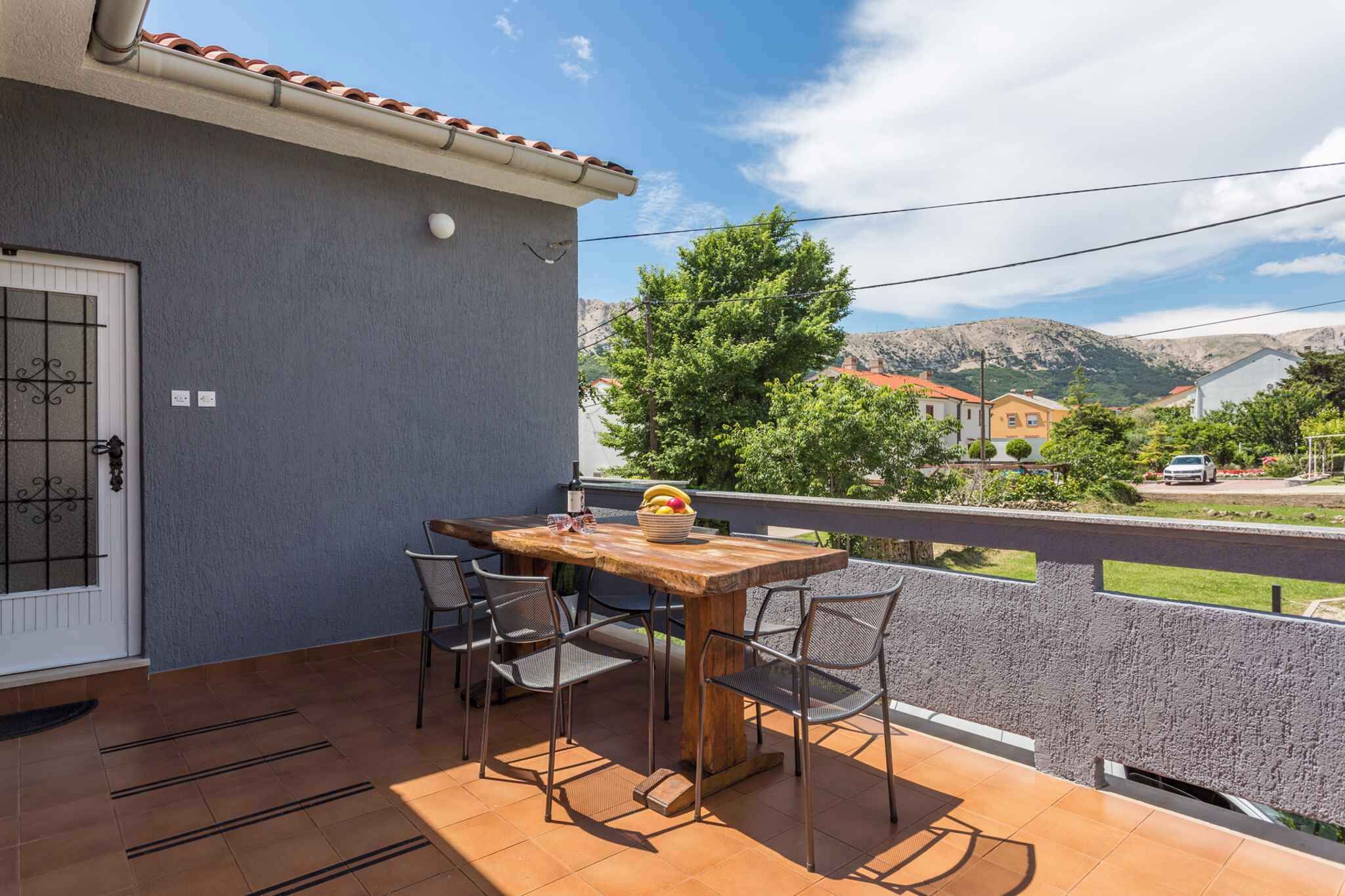 Un balcón con mesa y sillas de madera, piso de baldosas y vista a un paisaje montañoso.