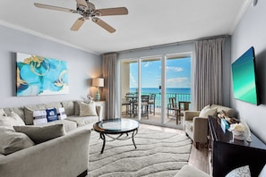 A hotel room with a balcony, a ceiling fan, a round glass table, and a large painting.