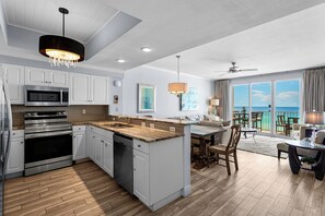 A modern kitchen with a central island, stainless steel appliances, and a dining area with a view of the ocean.