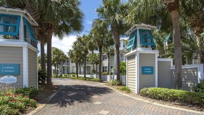A gated entrance to Gulfside Cottages with a paved walkway, palm trees, and a clear sky. - Eden's Estate - Pet Friendly, Heated Community Pool, Bikes Included! (Miramar Beach)