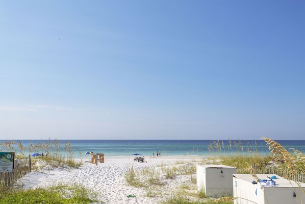 A beach with white sand, a few people, and a clear blue sky.