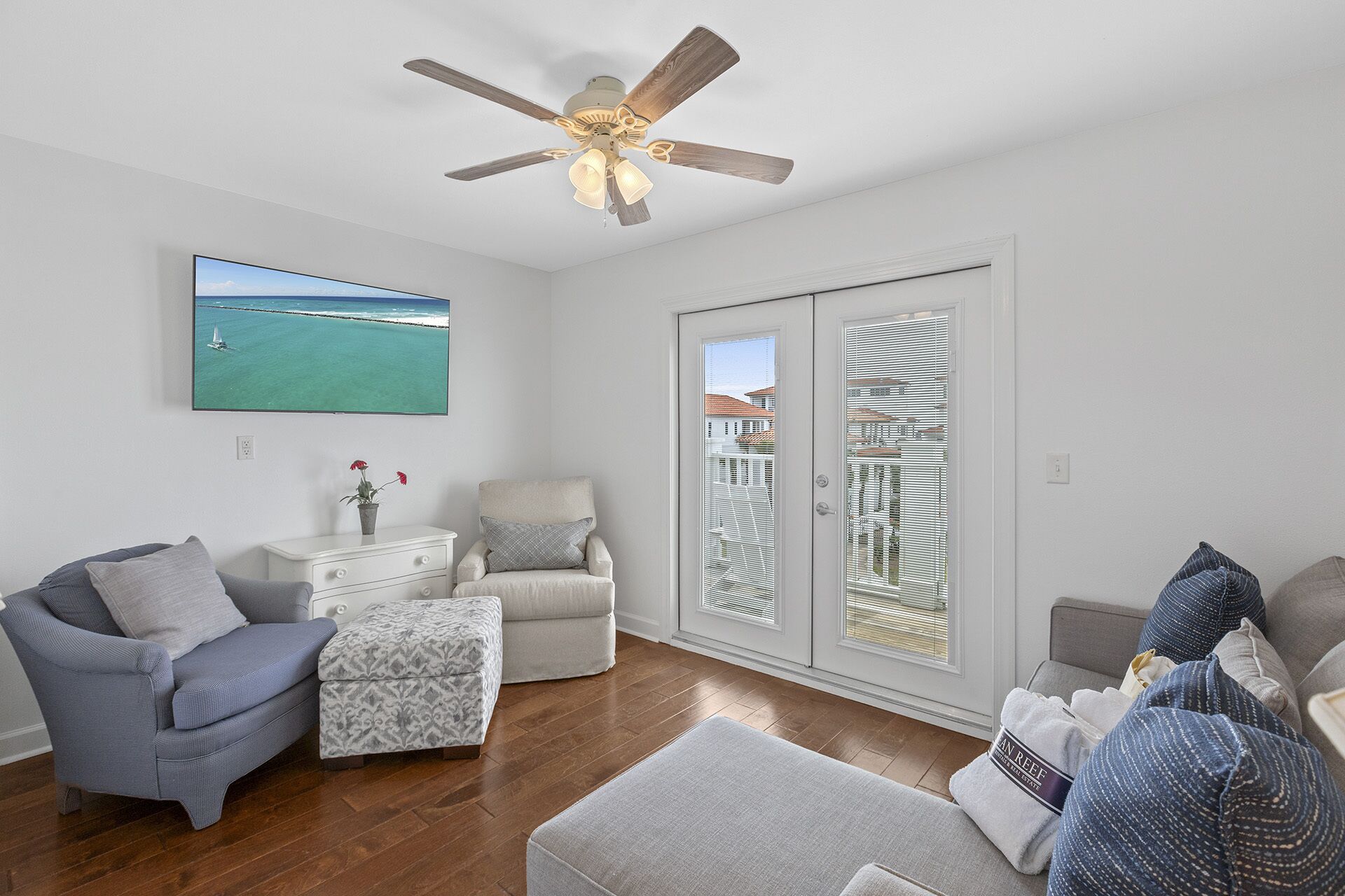 Un salon doté d’un ventilateur de plafond, d’un téléviseur diffusant un paysage, d’un canapé, d’un fauteuil et d’une petite table sur laquelle est posée une plante.