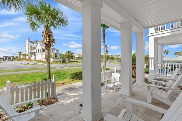 A covered porch with white chairs and a white picket fence.