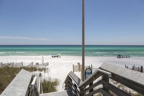 A beach with a wooden boardwalk leading to the shore, clear blue water, and a few beachgoers.