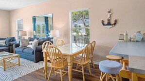 A living room with a sofa, a dining table with chairs, and a large window with blinds. - Legends 310 - Santa Rosa Beach, Community Pool, Hot Tub, Tennis Courts! (Santa Rosa Beach)