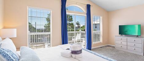 A hotel room with a bed, a TV, a dresser, and a balcony with blue curtains.