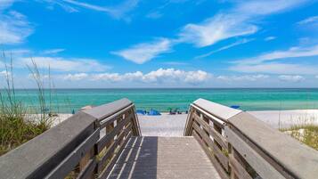Een houten looppad leidt naar een strand met helder turquoise water en een blauwe lucht.