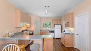 A compact kitchen with wooden cabinets, a central island with stools, a refrigerator, and a microwave. - Legends 310 - Santa Rosa Beach, Community Pool, Hot Tub, Tennis Courts! (Santa Rosa Beach)