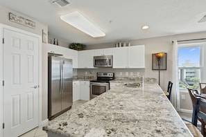 A modern kitchen with white cabinets, stainless steel appliances, and a granite countertop. - Amalfi Coast 412A - Gulf Views! Community Pool! Fitness Facility! Tennis Courts! (Miramar Beach)