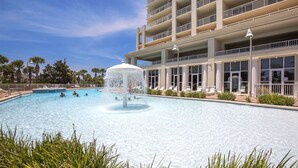 A swimming pool with a central fountain, surrounded by lounge chairs and a multi-story building with balconies.