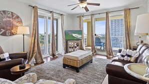 A spacious living room with a large window, a ceiling fan, and a television.
