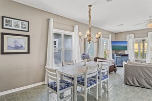 A dining area with a white table and blue cushioned chairs, a chandelier, and framed artwork on the wall.