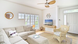 Un salon comprenant un canapé, un pouf, un fauteuil en osier, un téléviseur et un ventilateur de plafond.