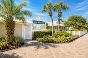 Crystal Beach Cottages with a white fence, palm trees, and a paved walkway.