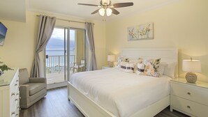 Hotelkamer met een bed, nachtkastje, stoel, plafondventilator, schilderij en uitzicht op de oceaan.